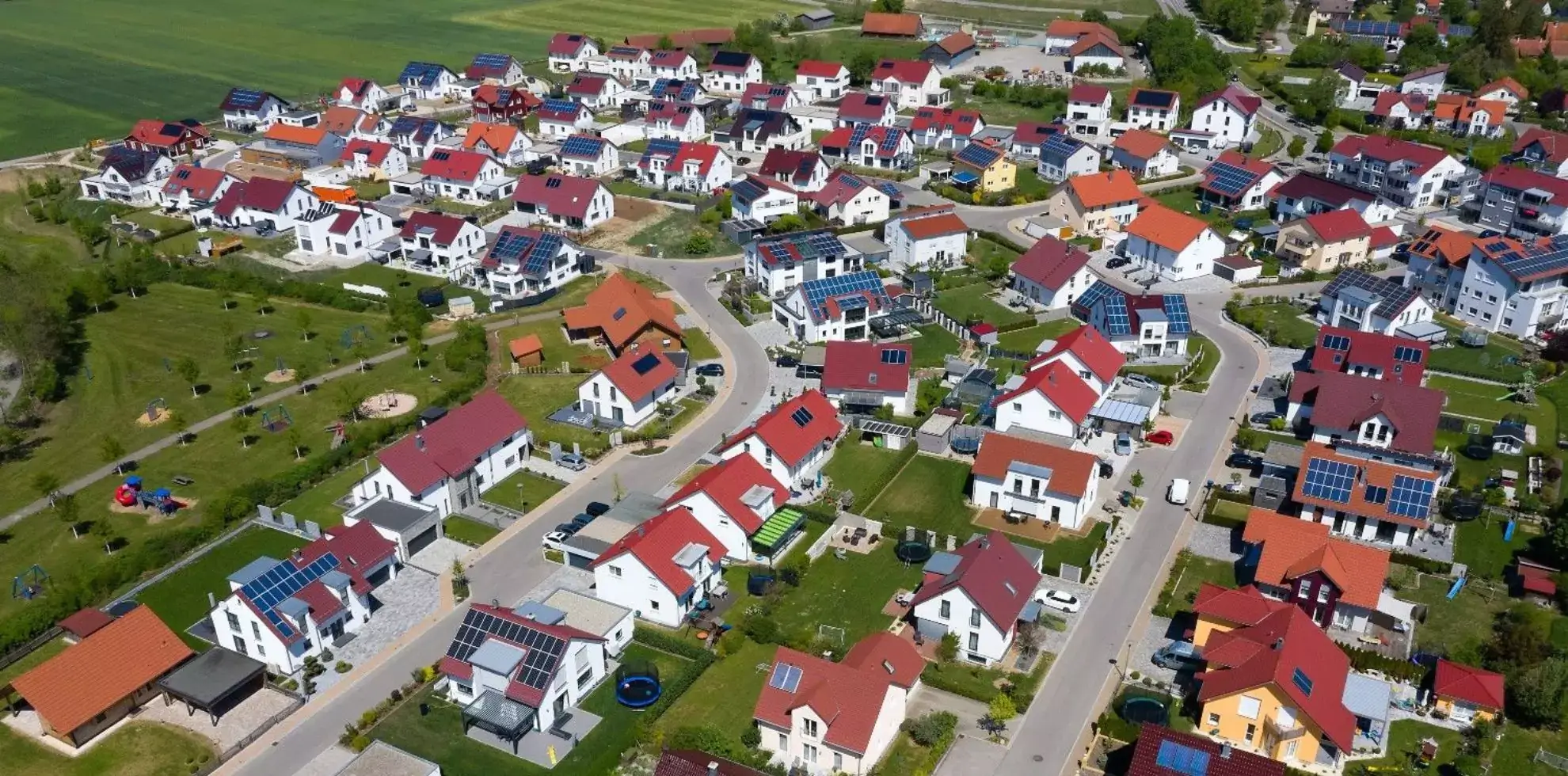 UK houses making the transition to net zero. A ariel view of a small housing estate. Most houses have red roofs and the estate is surrounded by fields. Most houses have solar panels.